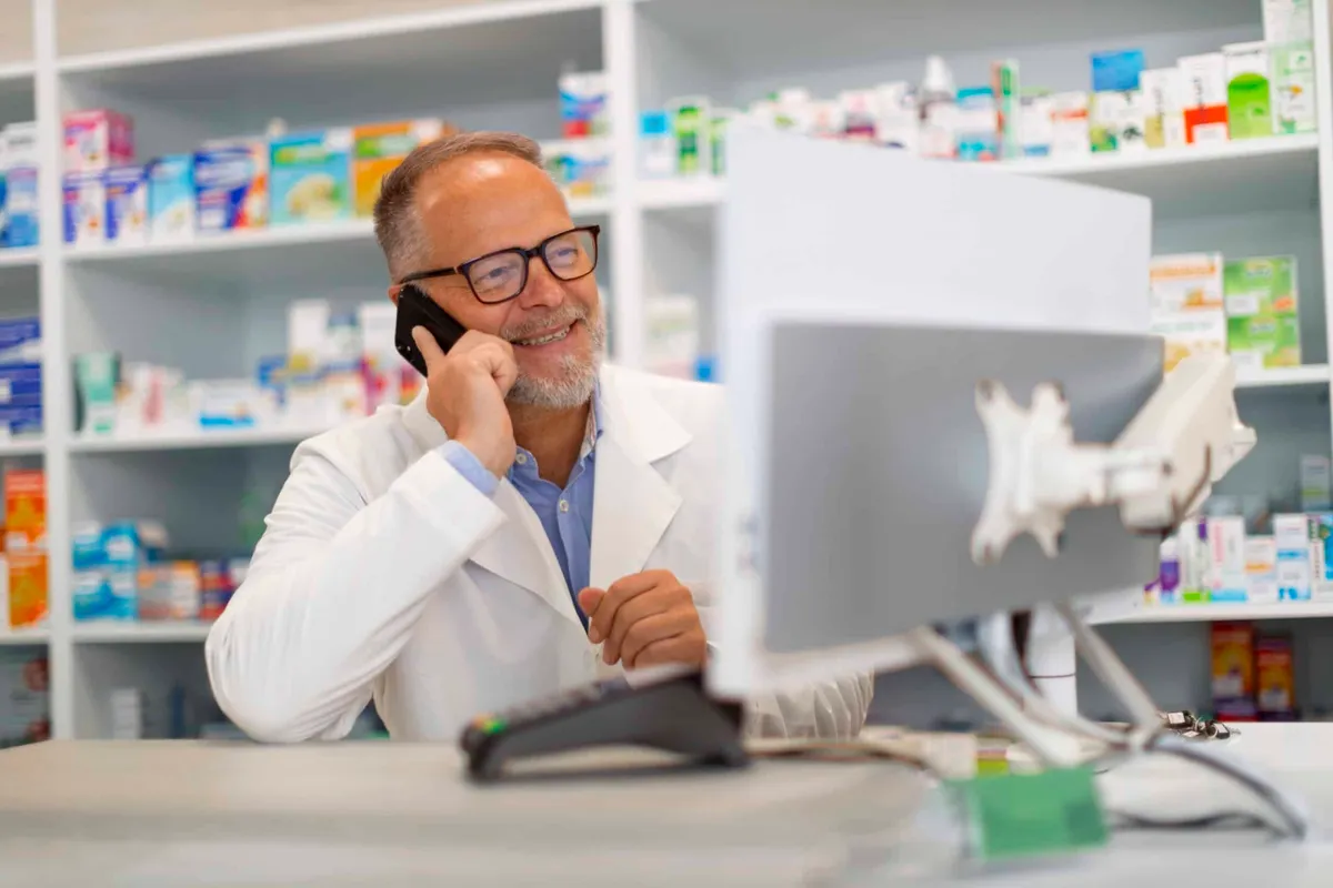 A community pharmacist taking a call at his pharmacy counter